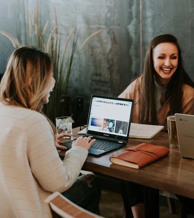 Three people working together and smiling at a table with laptops